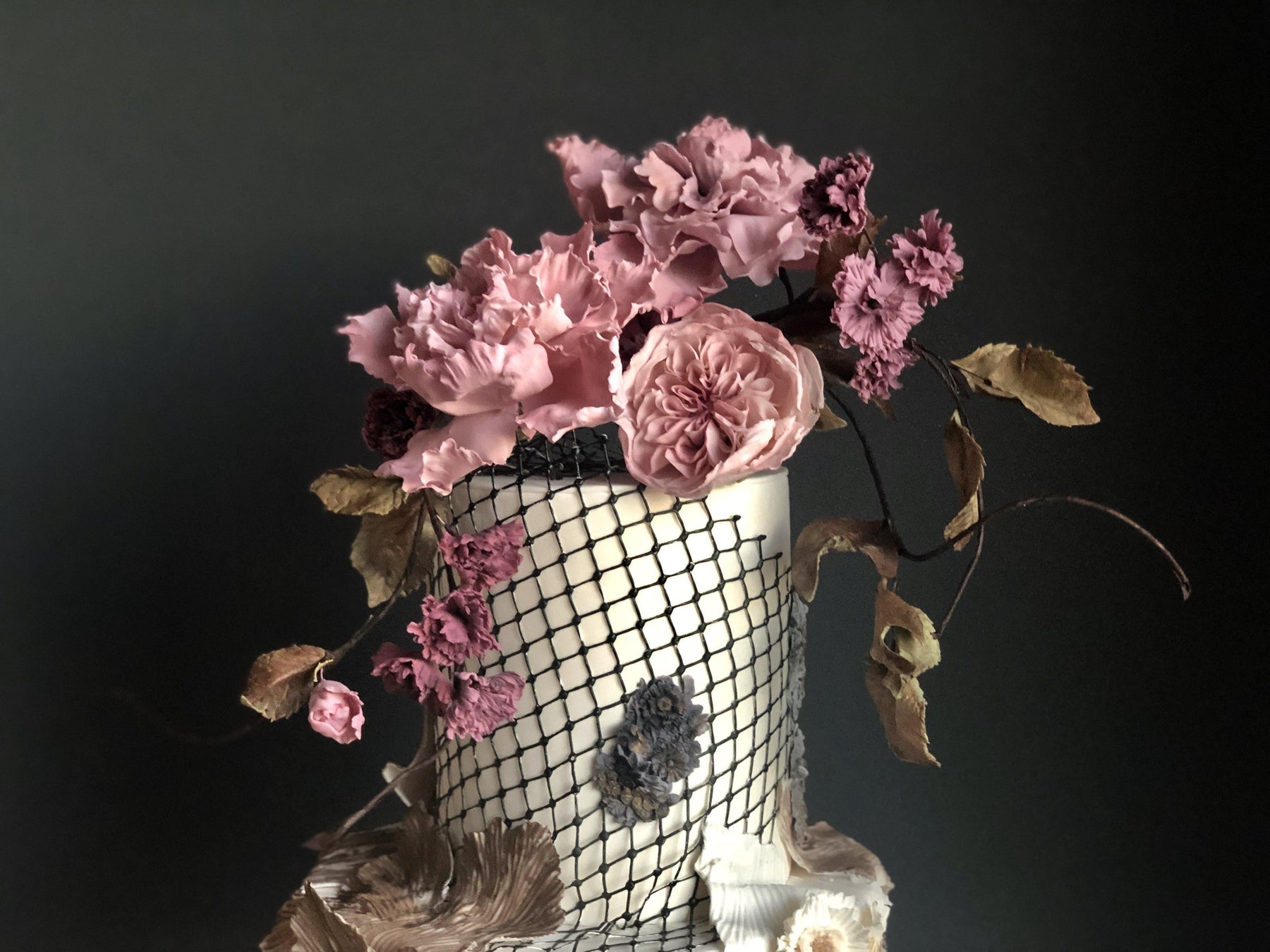 Elegant wedding cake with pink sugar flowers, a black net design, and delicate leaves.