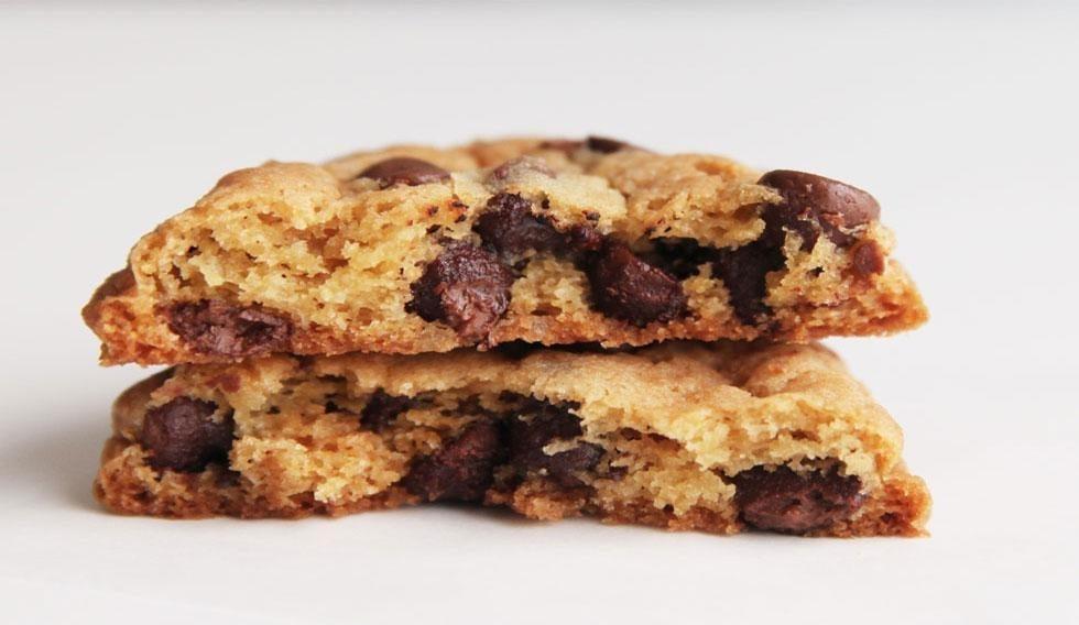 Two chewy, golden-brown chocolate chip cookies stacked, revealing a soft interior with melted chocolate.
