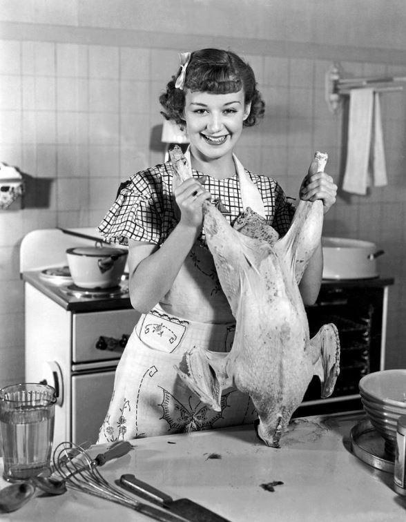 Smiling 1950s woman in an apron proudly holds up a raw turkey in a retro kitchen.
