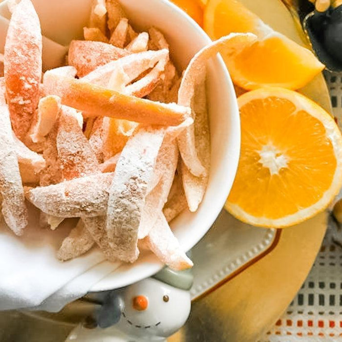 White bowl overflowing with sugar-dusted candied orange peels, next to a fresh orange half.