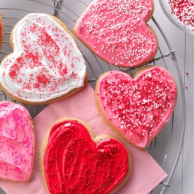 Heart-shaped cookies with red, pink, and white icing, decorated with sprinkles on a cooling rack.
