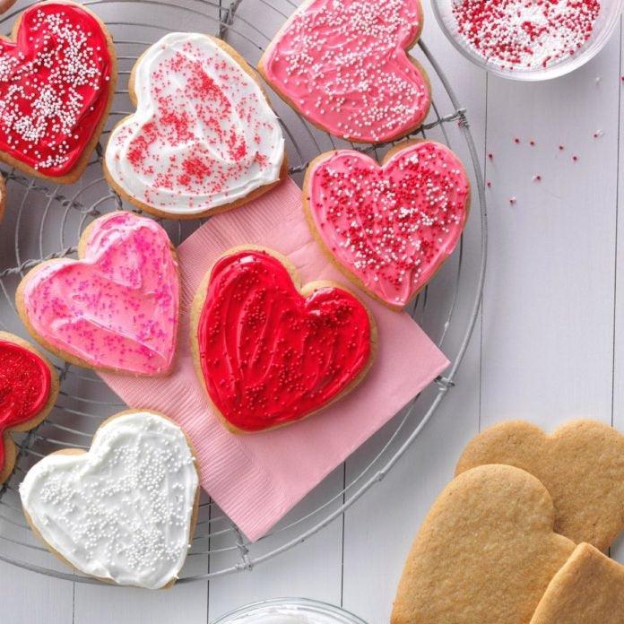 Heart-shaped sugar cookies with red, pink, and white icing and sprinkles on a cooling rack.