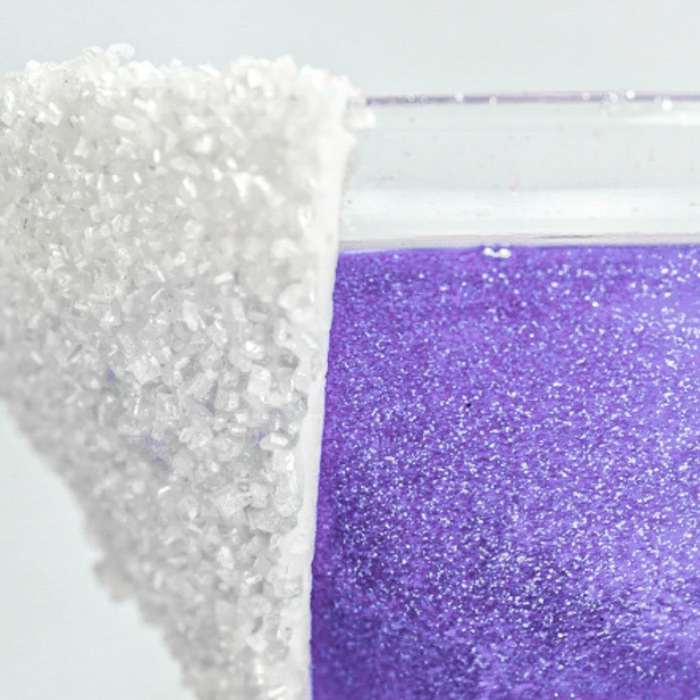 Close-up of a glass with a sparkling purple drink and a white sugar-rimmed edge.