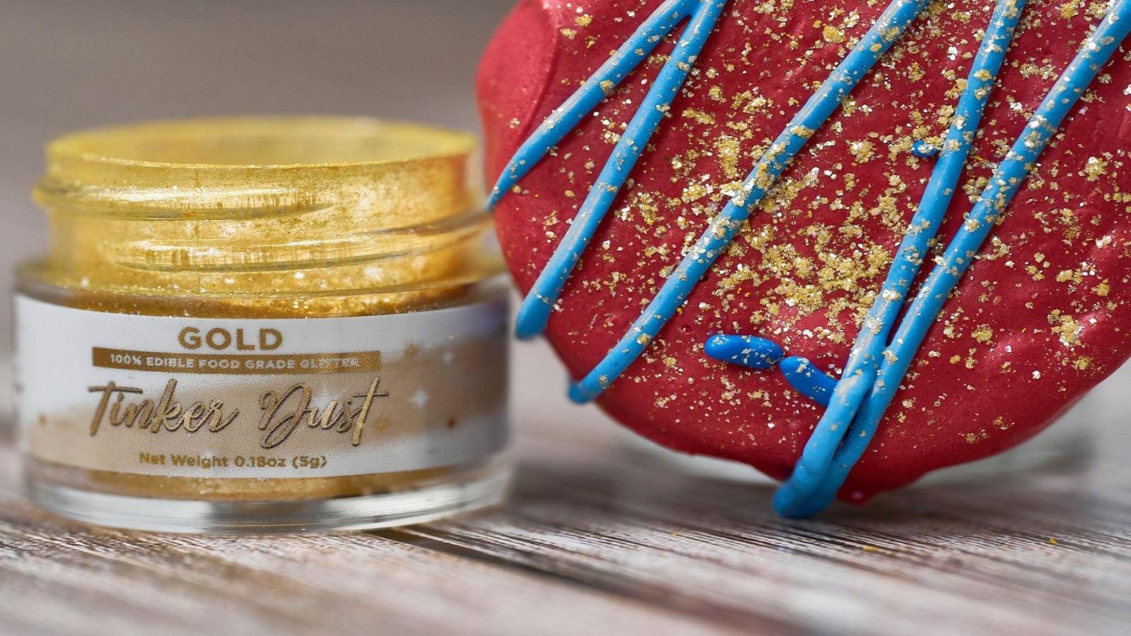 Jar of "Tinker Dust" edible gold glitter next to a red dessert with blue icing and gold sprinkles.