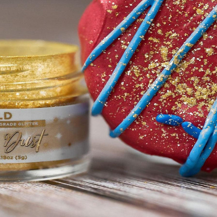 Jar of "Tinker Dust" edible gold glitter next to a red dessert with blue icing and gold sprinkles.