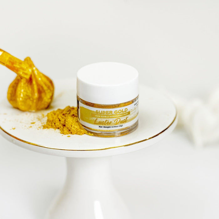Super Gold Luster Dust jar with a pile of edible gold dust and a gold-painted pastry brush.