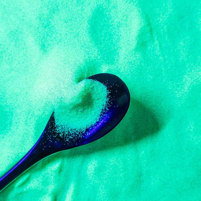 Ultrafine UV reactive iridescent craft glitter in a vibrant baby yellow, scooped by a dark spoon.
