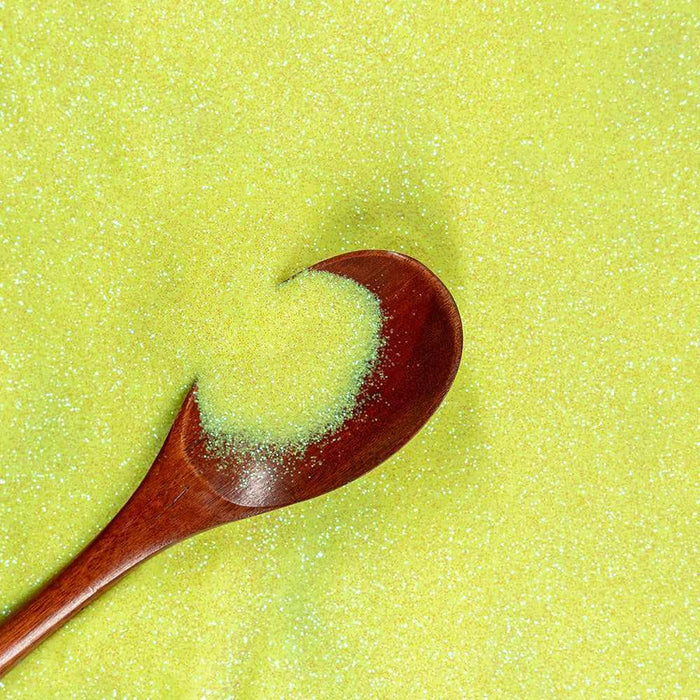 Baby yellow ultrafine UV reactive iridescent craft glitter in a wooden spoon on a glitter background.