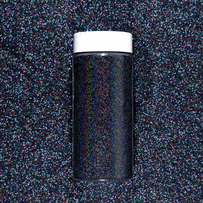 Black Magic Ultrafine Holographic Craft Glitter Dazzler Dust in a clear jar with a white cap, on a glitter background.