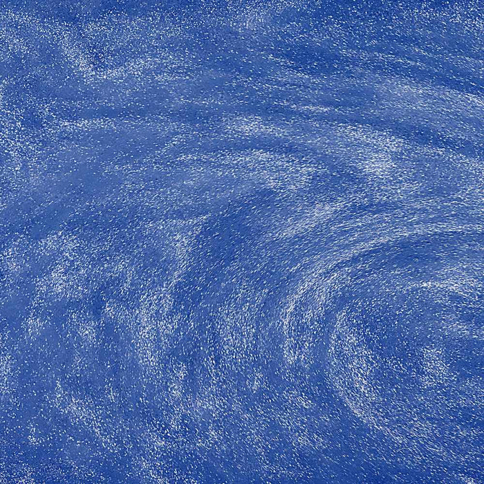 Swirling blue edible glitter particles suspended in a liquid, creating a shimmering, sparkling effect.