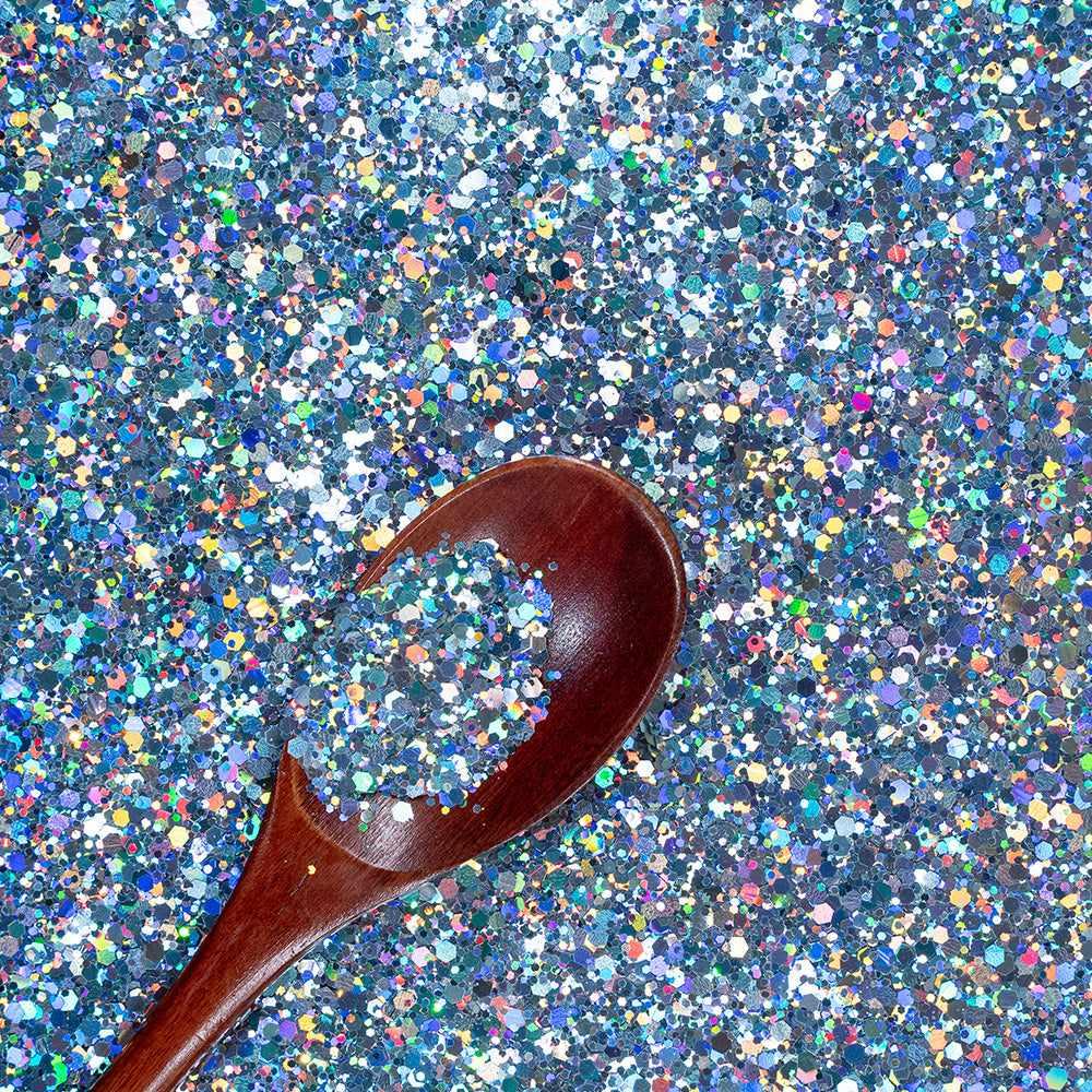 Chunky rainbow holographic hexagon craft glitter in blue tones with a wooden spoon.