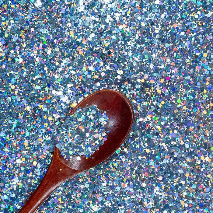 Chunky rainbow holographic hexagon craft glitter in blue tones with a wooden spoon.