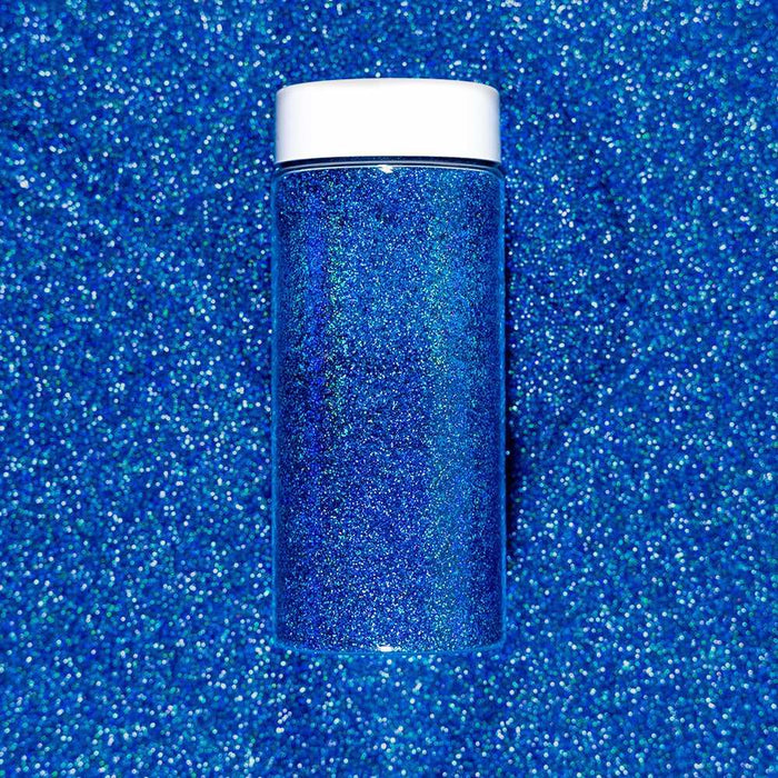Deep Ocean Blue ultrafine holographic craft glitter in a clear jar with a white lid, on a sparkling blue background.