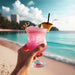 pink shimmer tropical cocktail held up at the beach