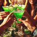 a round people holding green glitter cocktails at a party