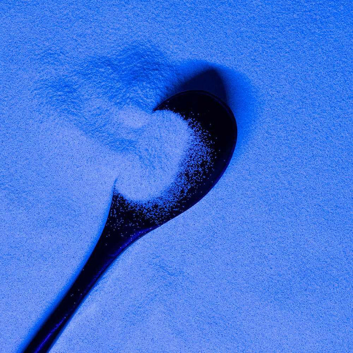 Ultrafine matte UV reactive craft glitter, snow white Dazzler Dust, on a dark spoon under blue light.