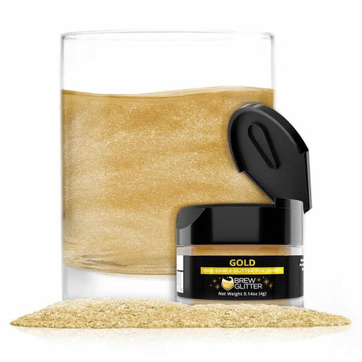 Gold edible Brew Glitter in a 4g jar with an open lid, next to a glass of shimmering gold drink and a pile of glitter.