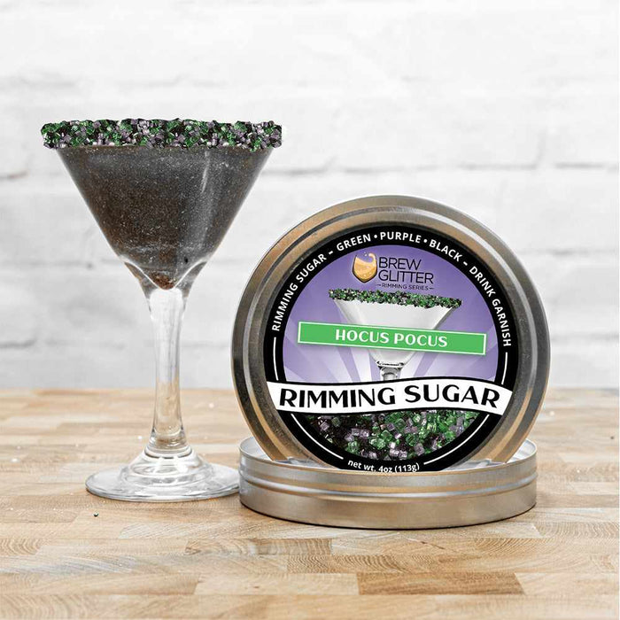 Hocus Pocus Rimming Sugar tin with green, purple, and black sugar, next to a martini glass with a black sugar rim.