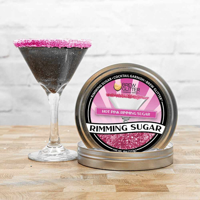 Hot pink rimming sugar in a metal tin next to a martini glass with a pink sugar rim.