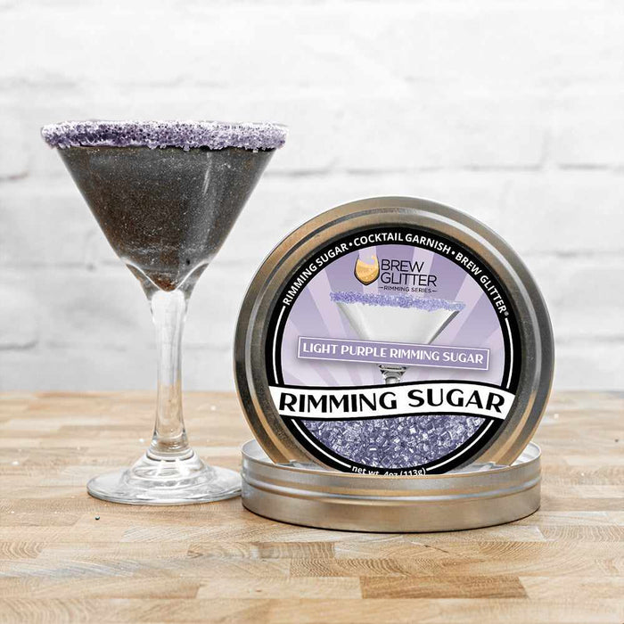 black glitter drink with a light purple sugar rim next to rimming tin