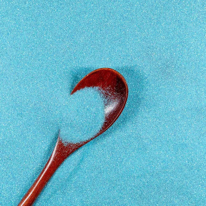 Light teal ultrafine iridescent craft glitter, Dazzler Dust, in a wooden spoon on a glitter background.