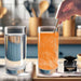 Hand stirring orange color-changing brew glitter into a tall glass of water next to a clear glass and a glitter jar.