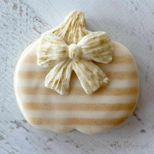 Pale gold luster dust on a striped pumpkin cookie with a matching bow.