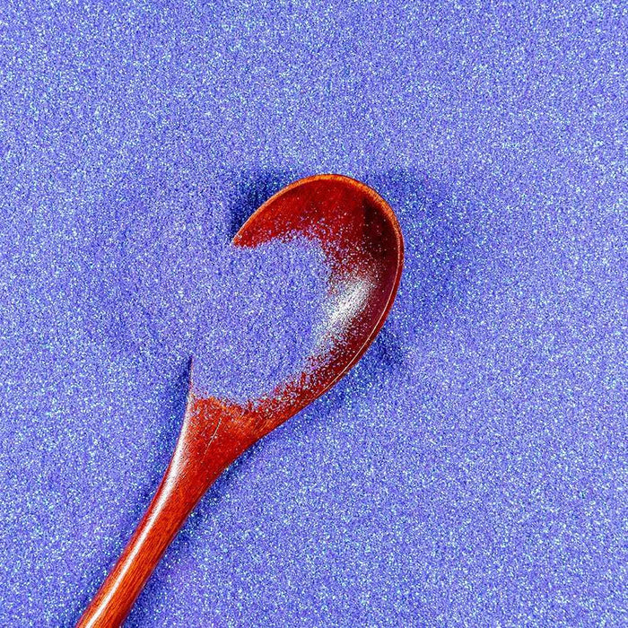 Pastel purple rainbow ultrafine iridescent craft glitter with a wooden spoon holding a small pile.