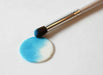 Periwinkle blue luster dust being applied with a brush to a white circular fondant piece.