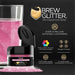 Pink Brew Glitter in a small black jar next to a glass of pink glittery drink.