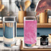 Hand stirring pink edible glitter into a glass of water next to a 4g jar of Brew Glitter on a kitchen counter.