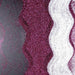Wavy lines of plum purple, dark purple, and white ultrafine metallic craft glitter.