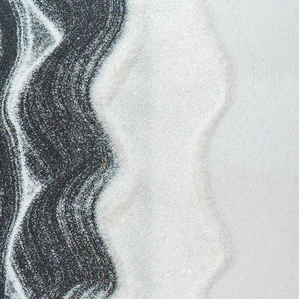 White iridescent craft glitter on a black and white background, creating wavy patterns.