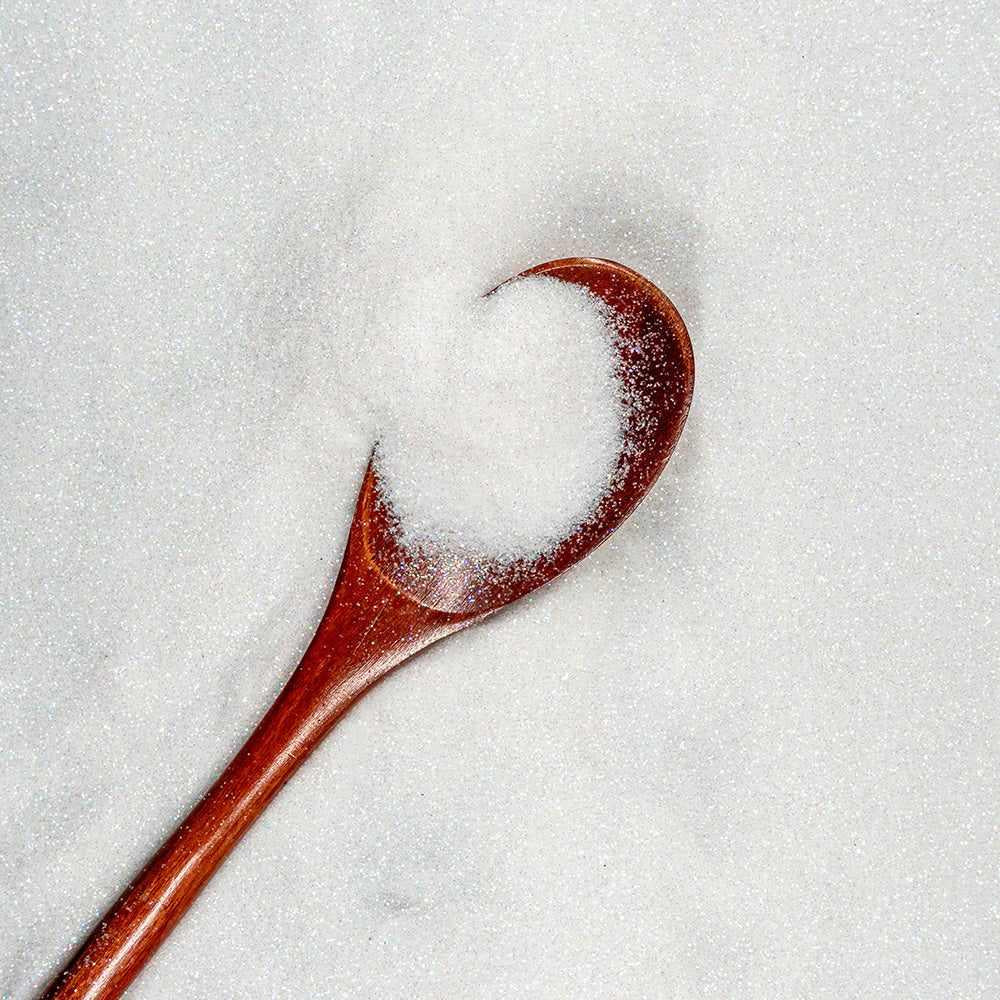 White iridescent craft glitter on a wooden spoon, surrounded by more glitter.