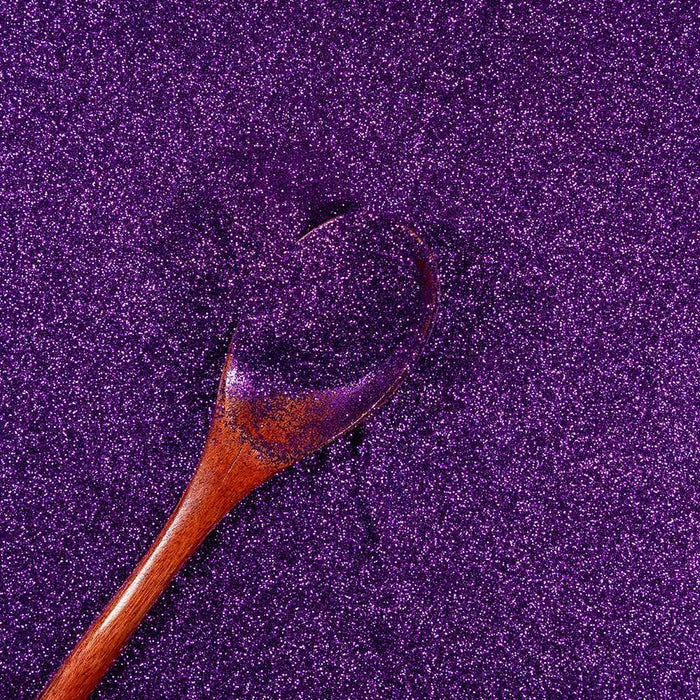 Royal Purple Ultrafine Metallic Craft Glitter Dazzler Dust with a wooden spoon scooping it.