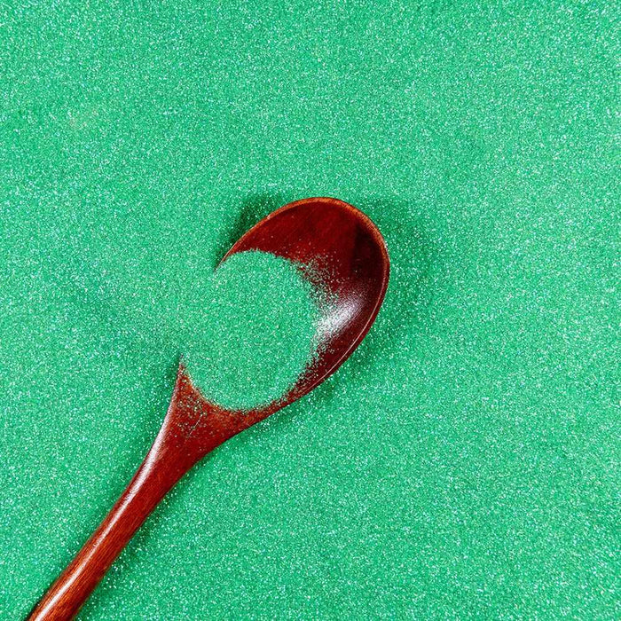 Sea green ultrafine iridescent craft glitter with a wooden spoon holding a small pile.