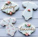White baby shower cookies decorated with pink and white roses and gold luster dust lettering.