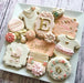 Assortment of decorated baby shower cookies in pink, white, and gold, featuring onesies, a stroller, and "Everly".
