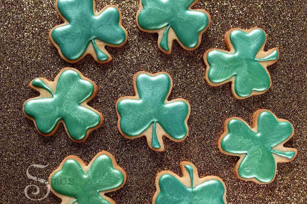 Spruce green luster dust on shamrock-shaped cookies, arranged on a glittery gold surface.