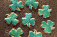 Spruce green luster dust on shamrock-shaped cookies, arranged on a glittery gold surface.
