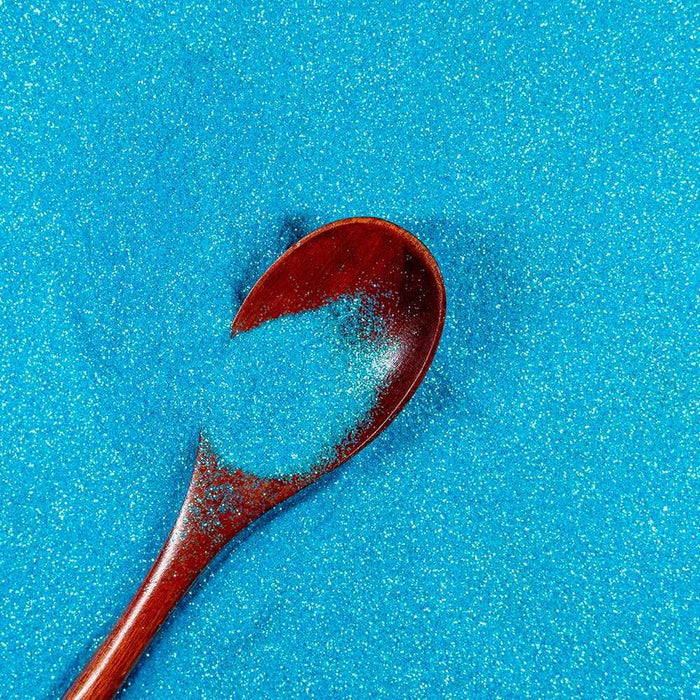 Teal blue ultrafine iridescent craft glitter with a wooden spoon holding some.