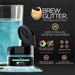 Teal Brew Glitter in a small black jar next to a glass of teal sparkling drink.