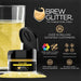 Yellow Brew Glitter in a small black jar, next to a glass of sparkling yellow drink.