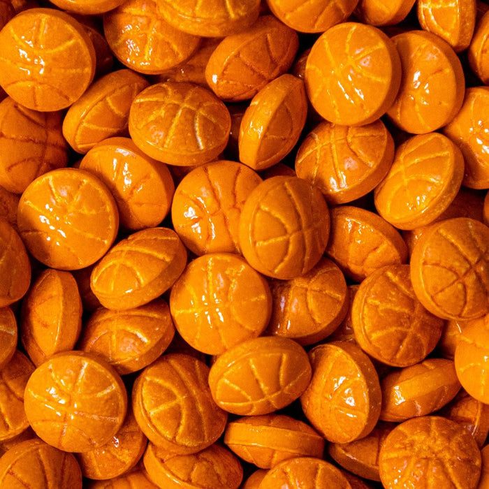 Close-up of vibrant orange, edible basketball-shaped sprinkles with embossed details.