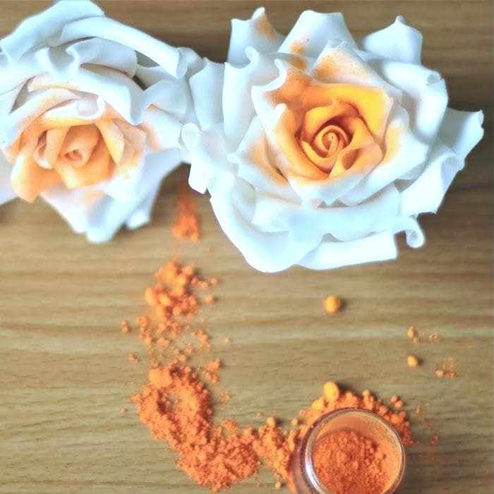 Classic Orange Luster Dust in a small jar, spilled on wood, with two white roses dusted orange.