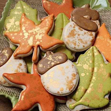 Assorted fall leaf and acorn cookies with orange, green, and white icing, speckled with gold luster dust.