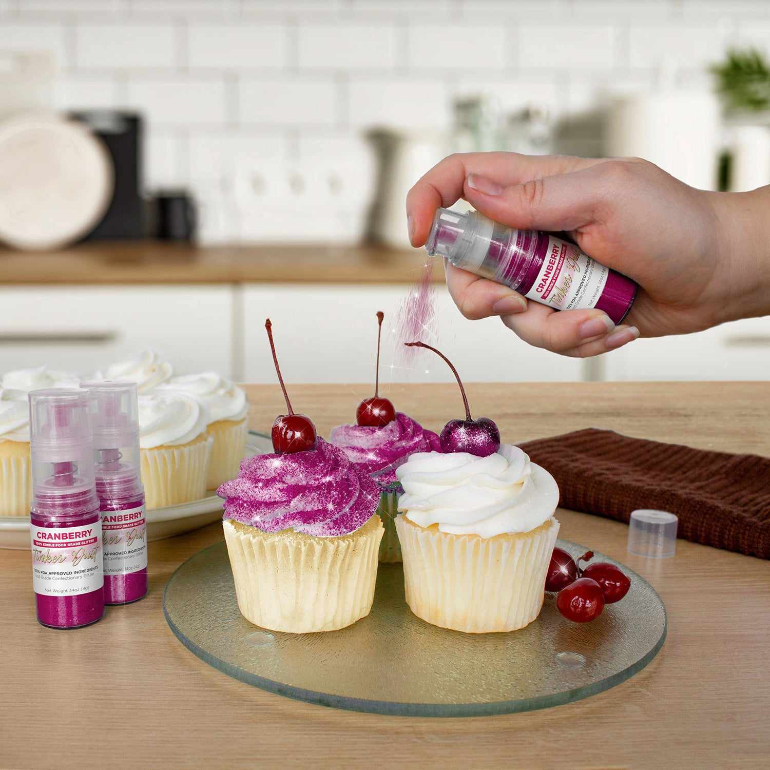 Three cupcakes being sprayed by a Cranberry color Edible Glitter 4 gram pump. | bakell.com