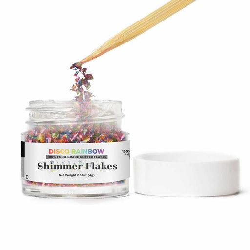Front view of an open jar of Disco Rainbow Edible Shimmer Flakes, with a wooden stick stirring the flakes | bakell.com