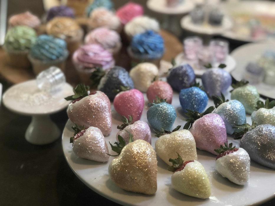 Assortment of glitter-dusted strawberries and cupcakes in various pastel colors, including pink, blue, and gold.