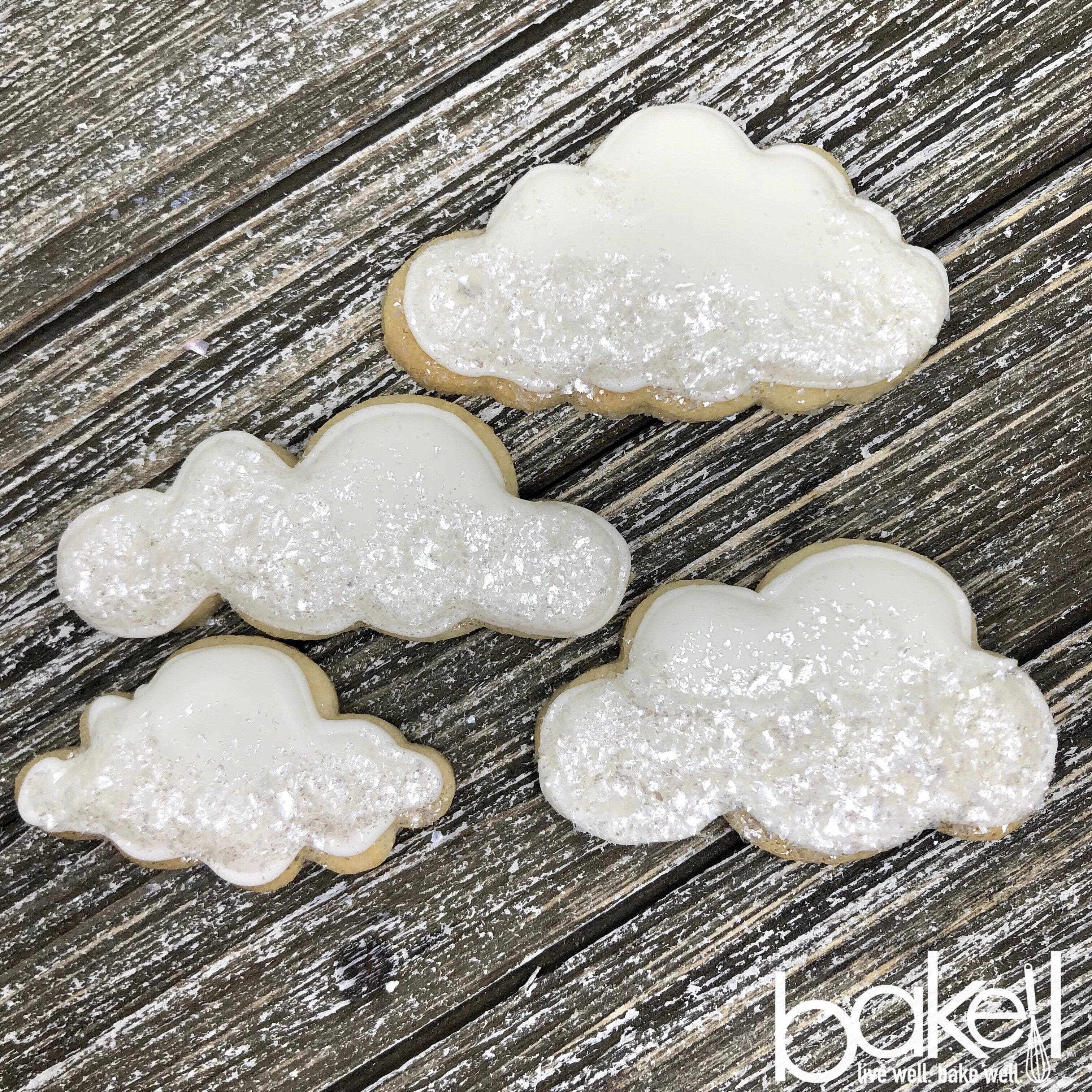 Ivory Tinker Dust® edible glitter on cloud-shaped cookies with white icing, on a rustic wooden surface.